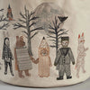 The Coral & Tusk Full Moon Masquerade Bucket features an embroidered scene on fabric, showcasing a variety of animals and figures in costumes at the Full Moon Masquerade. The detailed design includes a rabbit, a bear holding a notebook, a pencil, a person in a suit, and a mummy. They are depicted standing before bare trees and a large moon, with an owl and bat visible in the background.