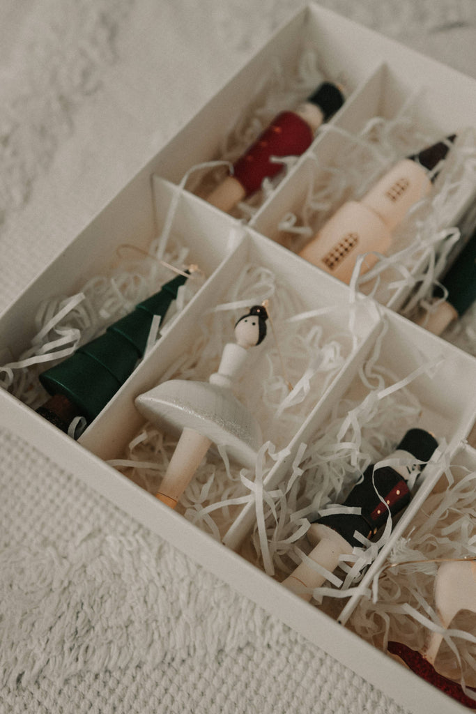 The Sabo Concept Christmas Ornaments come in a box with shredded paper and separate compartments, featuring hand-painted wooden pieces shaped like a ballerina, Christmas tree, nutcracker soldiers, and a house.