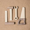 The Wooden Tool Set features four tools—a square, angle, wrench, and saw—crafted from solid rubber wood and Sapele teak. Each tool has a light body with a dark handle, displayed side by side on a corkboard background.
