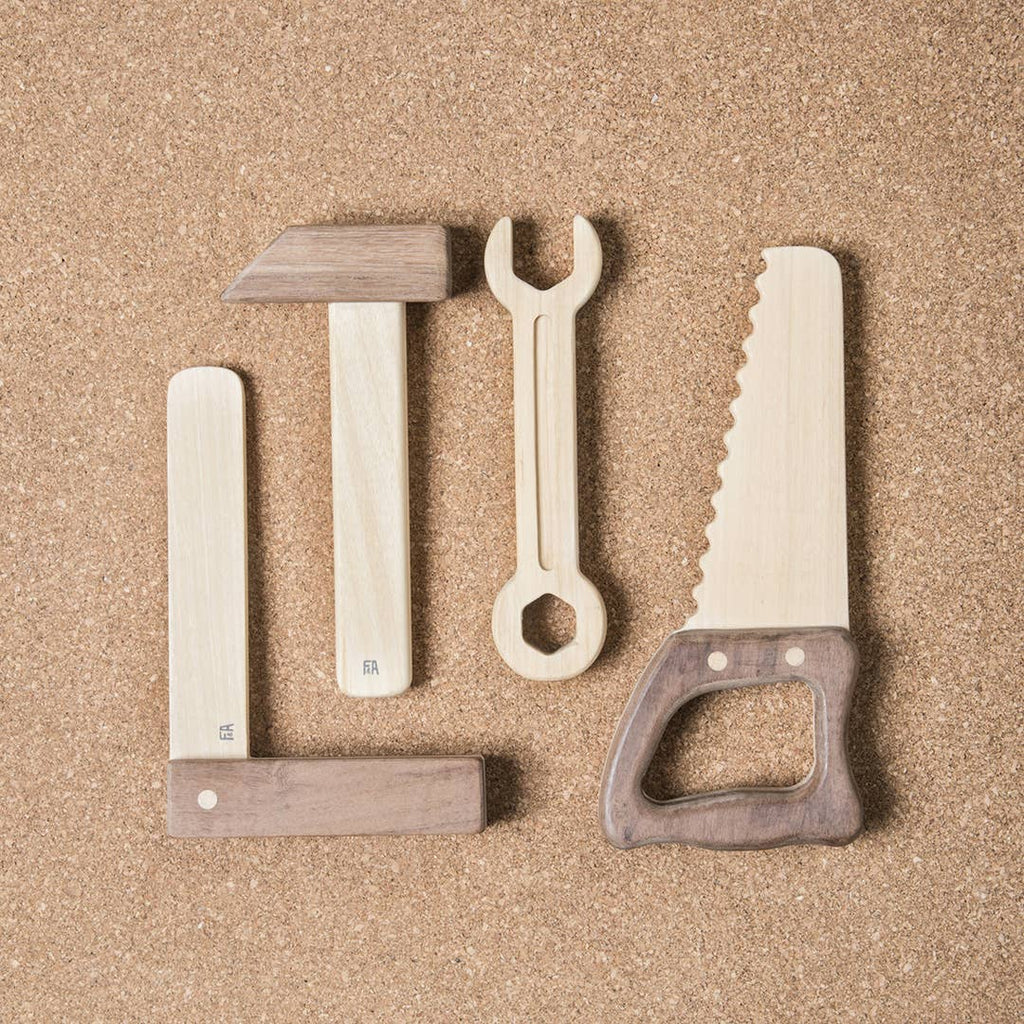 The Wooden Tool Set features four tools—a square, angle, wrench, and saw—crafted from solid rubber wood and Sapele teak. Each tool has a light body with a dark handle, displayed side by side on a corkboard background.