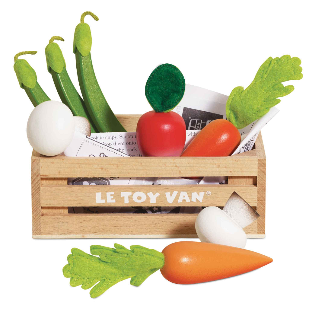 The Harvest Vegetables Wooden Market Crate by Le Toy Van features toy vegetables like a tomato, carrots, onions, and green beans around a wooden crate with newspaper-like paper inside to inspire imaginative play and promote healthy eating habits.