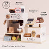 The Barista Café Shop (ships in one week) is a 17-piece wooden playset featuring a coffee machine, till, food display, pastries, drinks, barista accessories, and “Hand Made with Love” café charm for imaginative pretend play.