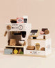 The Barista Café Shop, shipping in one week, is a wooden tabletop playset with a pretend espresso machine, cash register, loyalty card, plus play food such as chips, cookies, donut, lemon slices, and milk on a cream background.