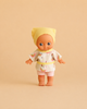 Introducing the Minikane Mini Pancha Doll - Alice with Unicorn Painting Outfit: a high-quality vinyl doll for imaginative play, featuring big blue eyes and dressed in a yellow headscarf, a white shirt adorned with colorful patterns, and white shorts, beautifully displayed on a beige background.
