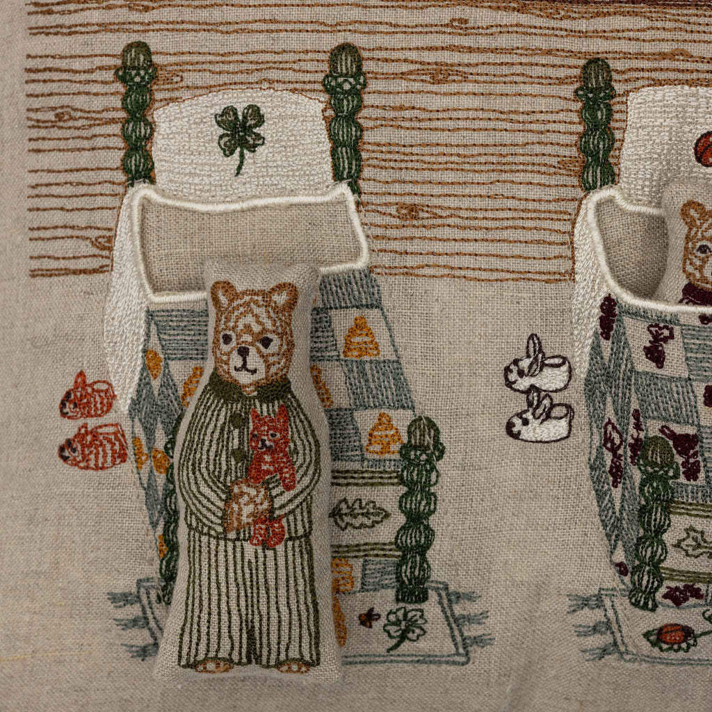 The Coral & Tusk Three Little Bears Pocket Pillow features an embroidered bear in striped pajamas by a patchwork quilt bed, with beds and rabbit toys in the background—perfect as a decorative kids pillow or storybook pocket. Ships in one week.