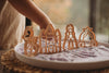 A child's hand reaches toward the Princess Cutter Set - Eco Playdough Tool—wooden, princess-themed figurines like a dragon, castle, princess, and carriage—displayed on a tray of purple sand and accompanied by eco-friendly playdough cutters and tools for imaginative storytelling.