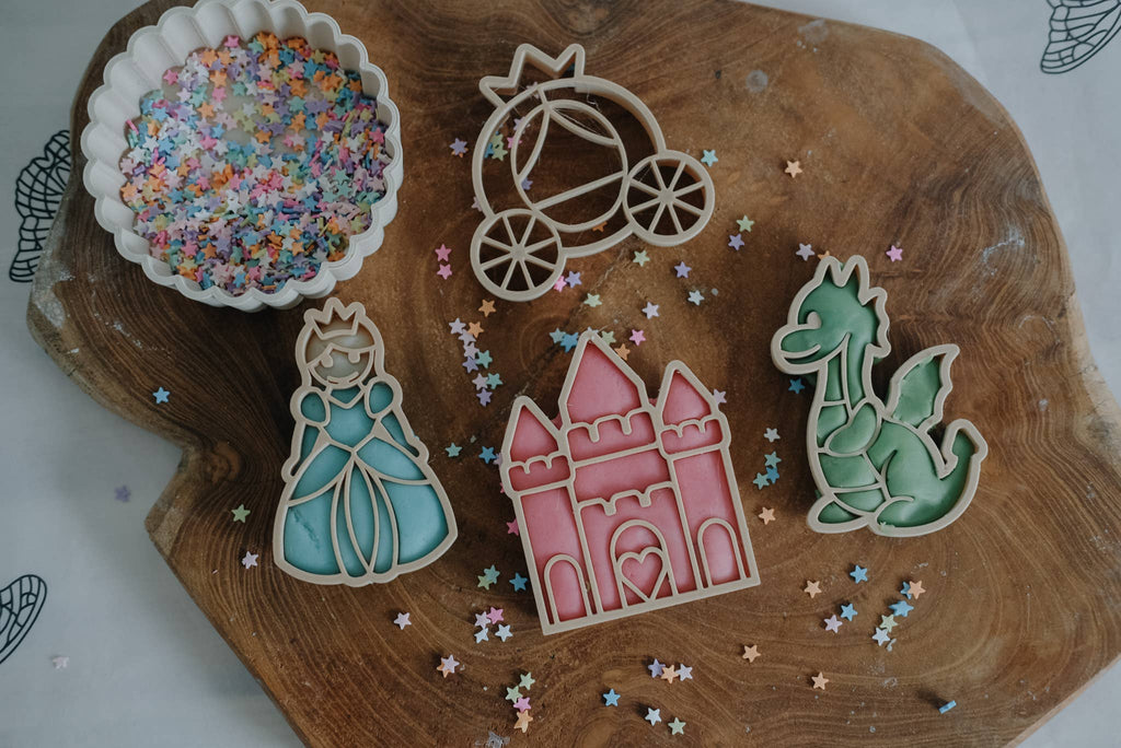 Sure! Here's a rewritten version using the given product data: A delightful assortment of decorated sugar cookies shaped like a princess, castle, carriage, and dragon are arranged on a wooden board alongside a bowl of vibrant star-shaped sprinkles and scattered loose sprinkles. This enchanting scene is perfect for sparking imaginative play—pair it with our Princess Cutter Set - Eco Playdough Tool to extend the magical adventures beyond snack time.