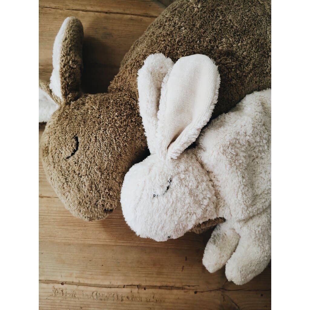 A Senger Naturwelt Cuddly Animal - White Bunny pillow with floppy ears and closed eyes lies on a wooden surface, creating a cozy and comforting scene.