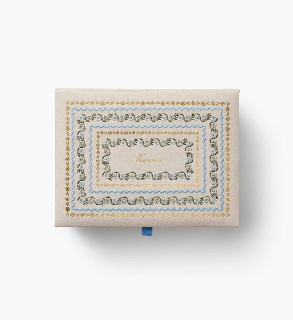The Delphine Large Embroidered Keepsake Box features ornate gold, blue, and green decorative borders with the word “Keepsakes” displayed in the center, showcased against a white background.