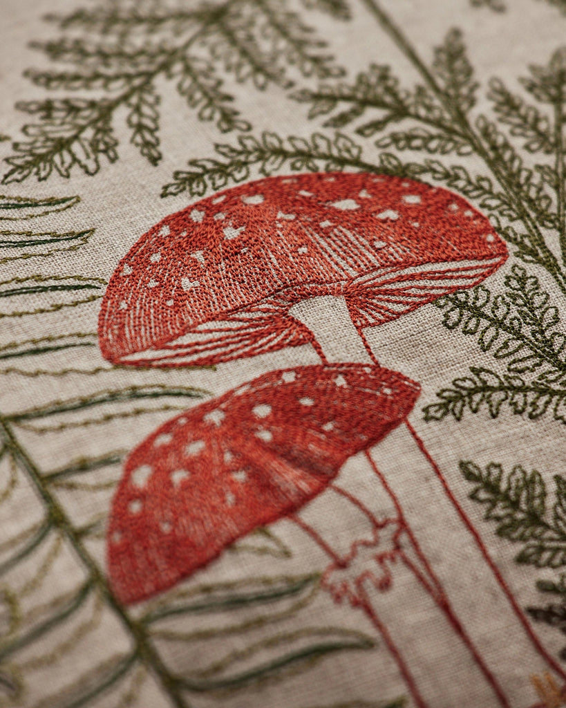 The Coral & Tusk Mushrooms and Ferns Lumbar Pillow showcases linen fabric embroidered with red mushrooms, white spots, and green fern leaves for a botanical, nature-inspired accent.