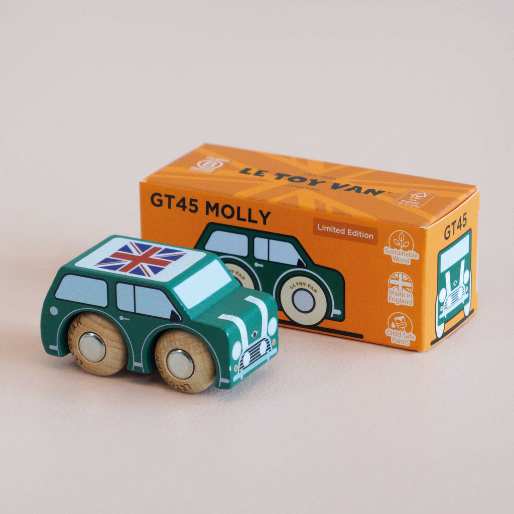 A small green wooden car with a Union Jack on the roof sits next to an orange box labeled “No. 7 GT45 Molly | Made in England.”.
