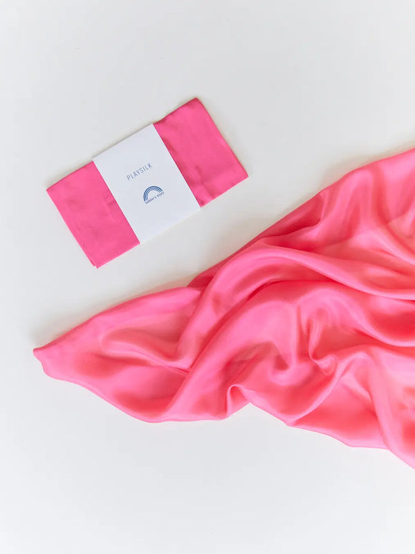 A pink Sarah's Silk Playsilk - Rose swirled gracefully next to a white and pink package labeled "pinkwell" on a white background.