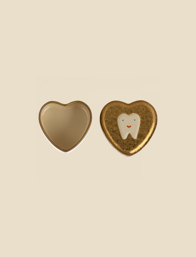 Two heart-shaped containers on a light beige background. The container on the left is open and empty, evoking childhood memories, while the one on the right is closed and features a white tooth with a smiley face on a golden background, perfect as a Maileg Tooth Box.