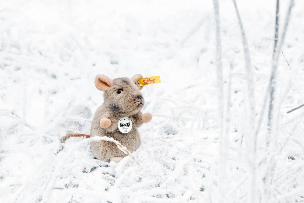 The Steiff Piff Mouse Plush Toy, 4 inches, with a tag on its ear, sits on snowy ground among frosty grass—an adorable collectible perfect for plush toy enthusiasts.