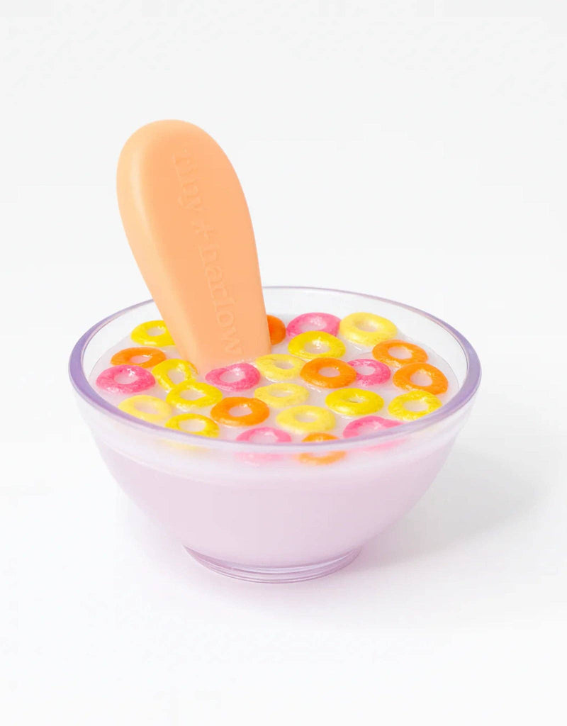 The Tiny Tummies - Tiny Loops Cereal Bowl features light purple milk with colorful round cereal—yellow, orange, and pink—and comes with an orange baby spoon. Set against a white background, it's perfect for a doll breakfast toy set.
