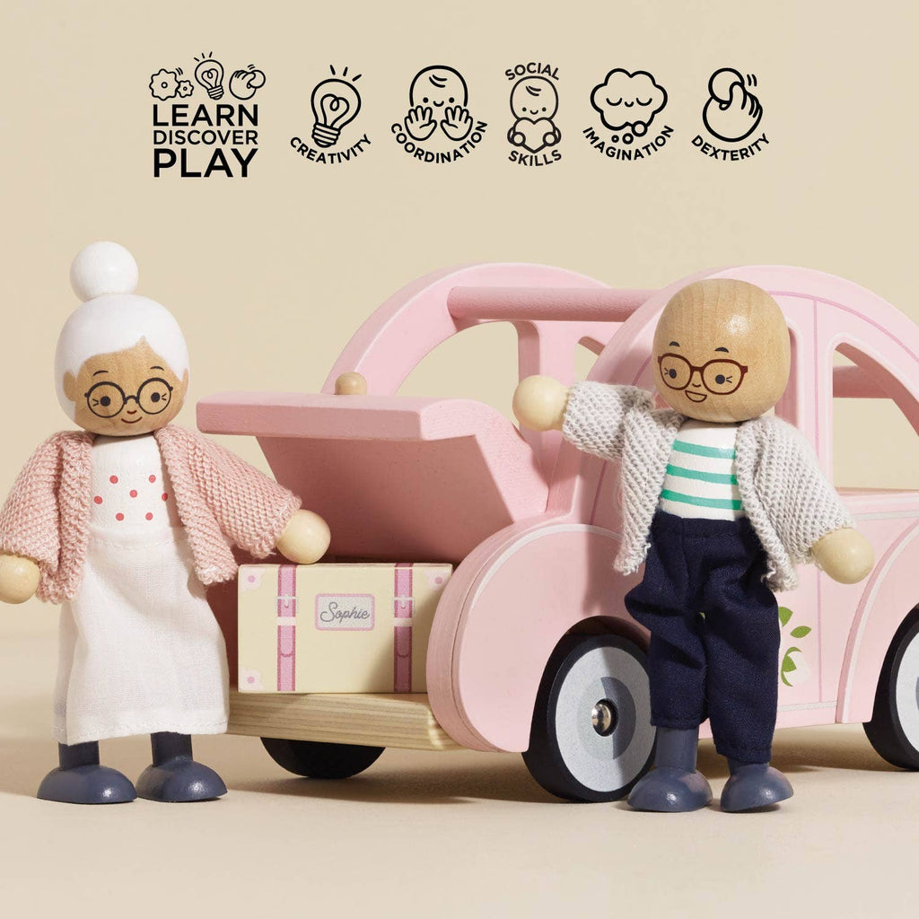Two wooden dolls, an elderly woman and man, stand by the Sophie's Dolls House Toy Car with an open trunk holding a suitcase. Icons above show its benefits: creativity, coordination, social skills, imagination, and dexterity.