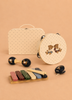 The Konges Sloejd Music Set - Teddy Bear is an adorable children’s instrument collection that includes wooden musical pieces like a tambourine, maracas, xylophone, and castanets, each adorned with cartoon bear designs and displayed in front of a lively polka-dot case on a soft beige backdrop.