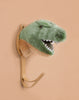 The Coat Hanger - T-Rex Dino is a wall-mounted hook with a plush green and beige dinosaur head featuring felt teeth, designed to resemble a T. rex, displayed against a plain beige background.
