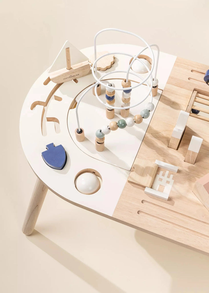 An overhead view of a modern Birch plywood Wooden Activity Table with various educational toys like beads, blocks, and shapes in soft neutral tones.