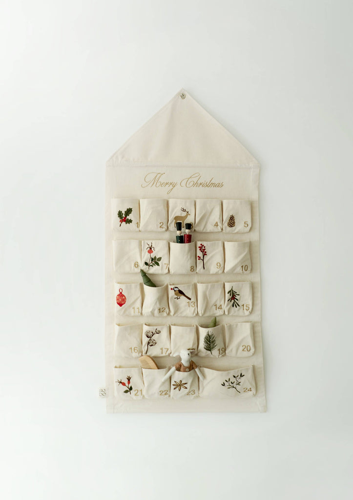 The Sabo Concept Christmas Cotton Advent Calendar features 24 cream-colored, cotton pockets with embroidered holly, presents, birds, trees, and “Merry Christmas” stitched above for a festive holiday display.
