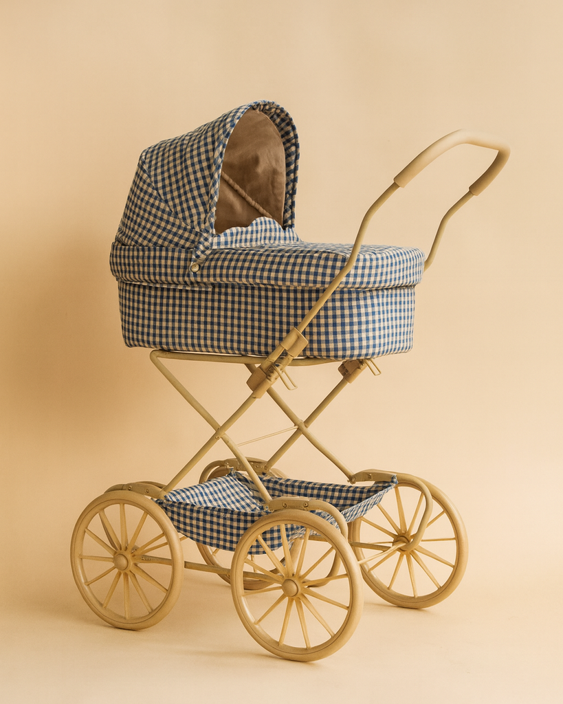 The Konges Sloejd Doll Pram - Blue Checkered features a vintage-style design with blue and white checkered organic cotton, a gold frame, and four large gold wheels, shown against a beige background.