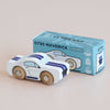 A white No. 17 GT95 Maverick toy car with blue racing stripes sits next to its matching blue box labeled “No. 17 GT95 Maverick | Made in England.” Inspired by a classic American muscle car, both the toy and the box share similar designs, and the car is finished with wooden wheels.