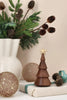 Spring Copenhagen The Christmas Tree, Thermo Beech, a small tiered wooden tree topped with a gold star, sits on a gift box, surrounded by two glittery gold ornaments and pine branches in a white vase.