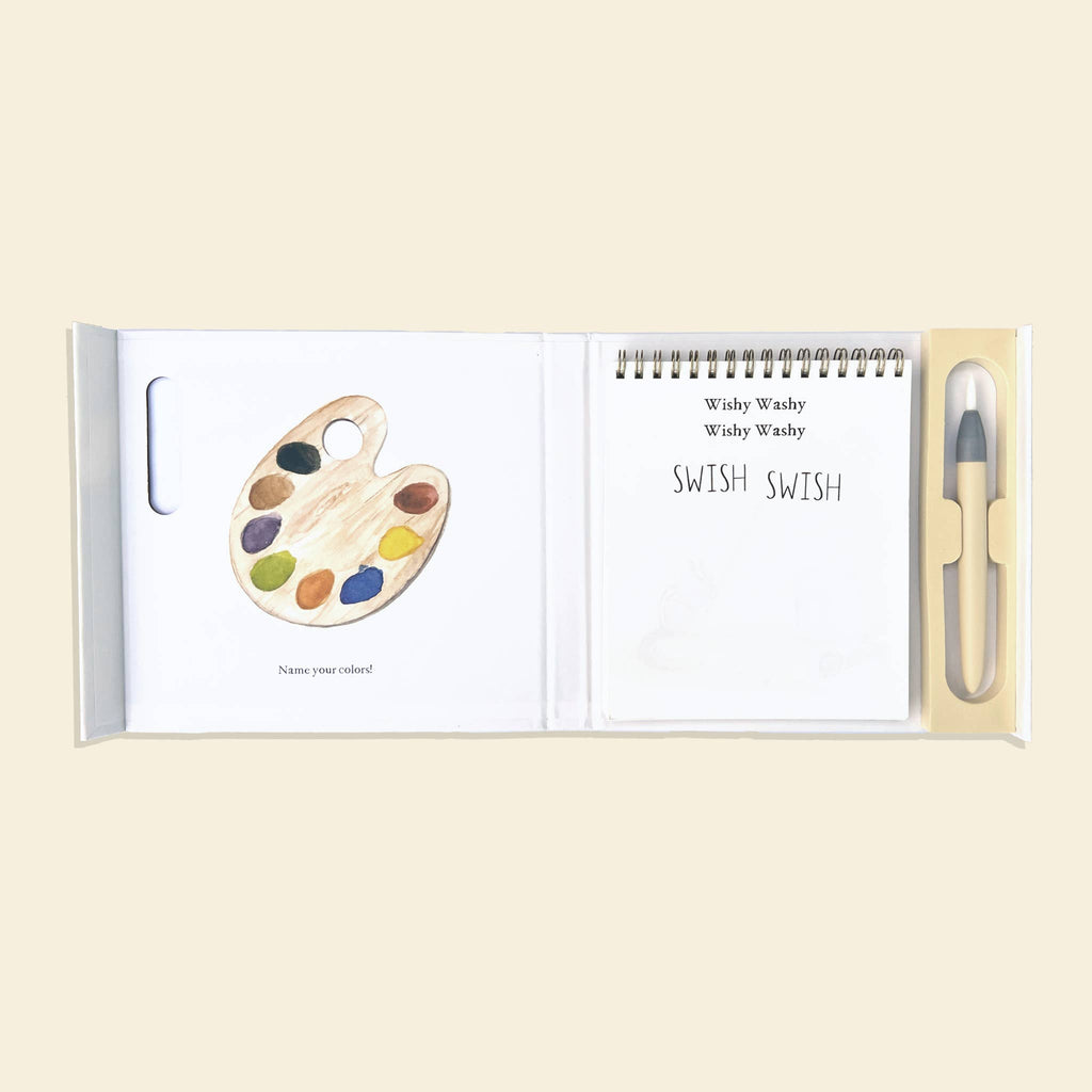 The Wishy Washy (Water Reveal Edition) is a perfect toddler travel activity, featuring a palette with paint colors, a notepad displaying “Wishy Washy Wishy Washy SWISH SWISH,” and a water brush pen.