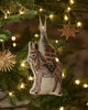 A Coral & Tusk Christmas Donkey Ornament featuring an embroidered donkey hanging on a Christmas tree, with a pack carrying a tree and a small bear.