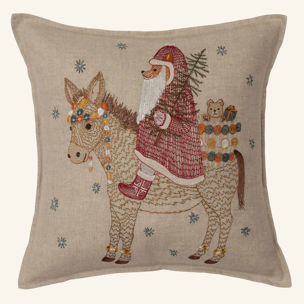 The Christmas Donkey Pillow features an embroidered donkey holding a Christmas tree with a toy basket holding a teddy bear. Snowflake patterns stitched around them complete the festive holiday décor.