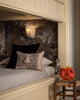 Cozy bunk bed with a Coral & Tusk Spooky Forest Pocket Pillow, wall lamp, and autumn wallpaper. A carved pumpkin lantern and mouse figurine rest on a wooden stool nearby.