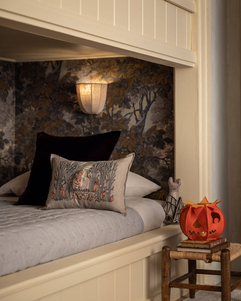 Cozy bunk bed with a Coral & Tusk Spooky Forest Pocket Pillow, wall lamp, and autumn wallpaper. A carved pumpkin lantern and mouse figurine rest on a wooden stool nearby.