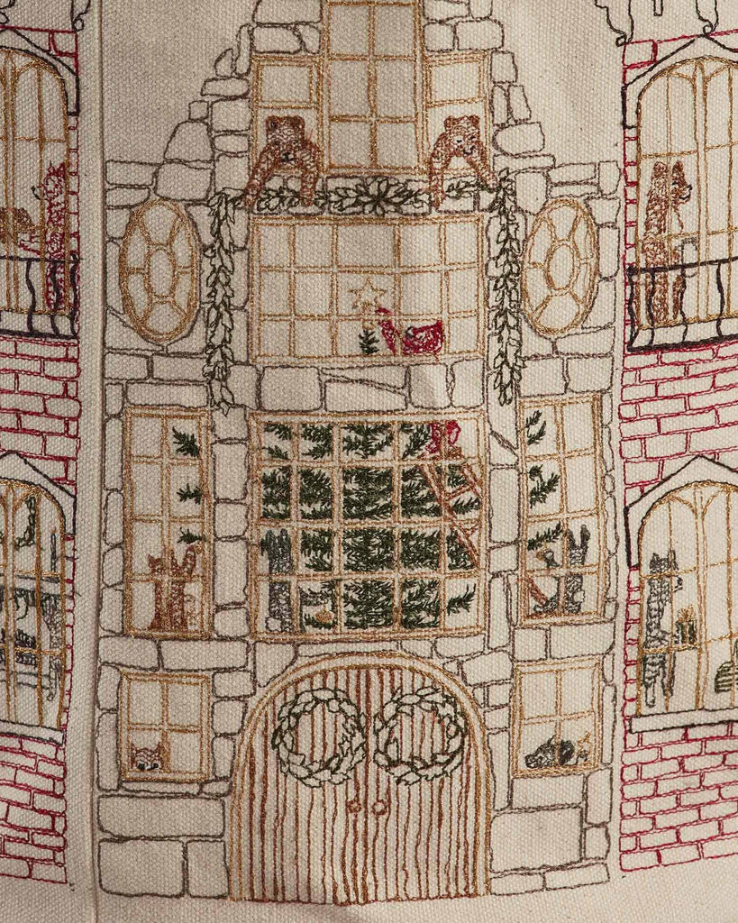 The Home for the Holidays Bucket features intricate embroidery of a tall house with large windows, a Christmas tree inside, wreaths on the door, and festive garlands—perfect for charming holiday storage or décor.