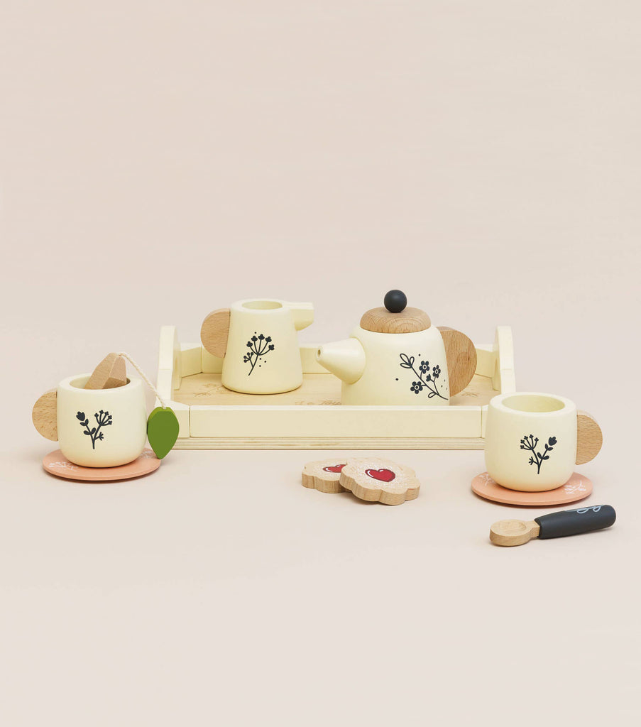 The eco-friendly Wooden Tea Set & Tray includes a floral-designed teapot, two cups, saucers, a tray, two heart-shaped biscuits, and a butter knife on a plain light beige background. Perfect for imaginative play, this charming set ships in approximately one week.