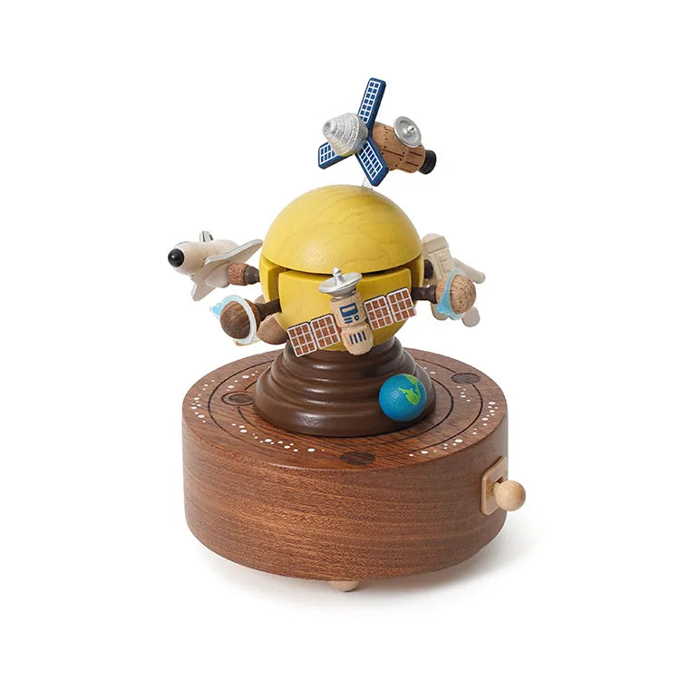 The Space Exploration Music Box features a yellow dome with satellites, rockets, and an airplane orbiting a small blue Earth, all set on a circular brown base with a hand crank.