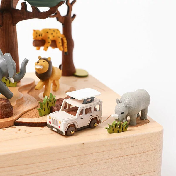 The Wooden Safari Music Box - Jeep Replacement showcases a white safari vehicle with Jeep-style details, plus a gray rhino, lion, cheetah, and elephant amid green grass and trees—all in a charming miniature design.