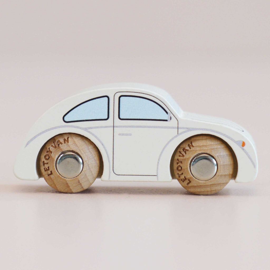 The No. 9 GT55 Betty, made in England, is a small classic wooden car featuring a white body, blue-tinted windows, and natural wood wheels that evoke the charm of a nostalgic toy—all beautifully presented against a soft beige background.