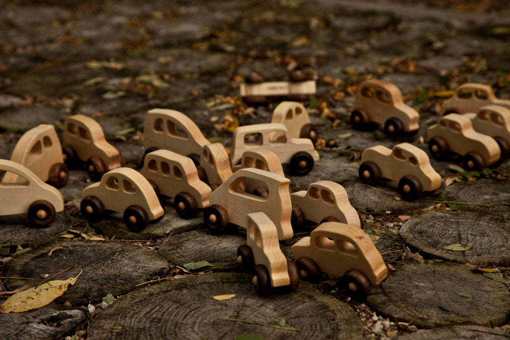 The Little Wooden French Car, an eco-friendly baby toy, lies on circular wooden slabs covered with fallen leaves.