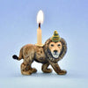 A small, decorative Lion Cake Topper shaped like a lion with a lit candle on its back, standing against a plain blue background. The lion features a detailed face, hand painted and sports a whimsical party.