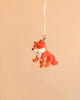 The Bukowski - Clever Fox Bag Charm, a small plush fox keychain, hangs from a cream-colored ribbon against a plain beige background.
