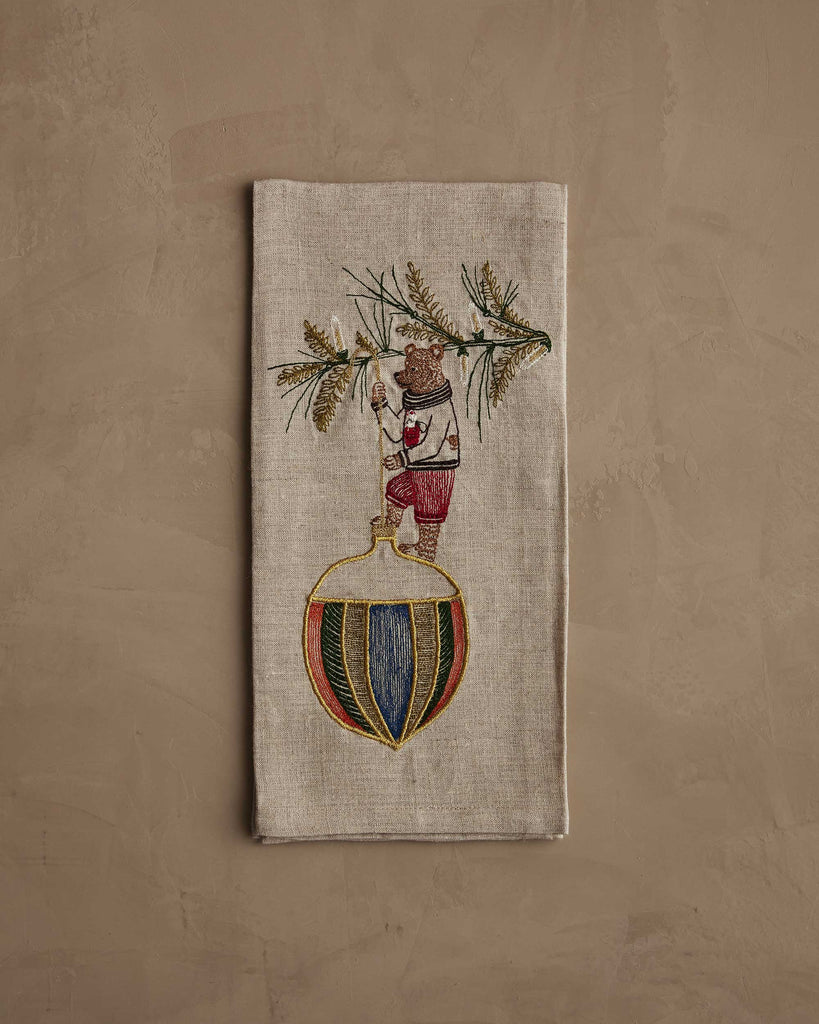 The Coral & Tusk Deck the Halls Bear Tea Towel showcases an embroidered bear in festive attire standing on an ornament with a pine branch, adding cheerful holiday charm to your kitchen décor.