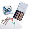 A Stockmar Triangular Coloured Pencil Set - 12 in a metal box with a peacock design on the lid, next to a drawing of a red and green flower on white paper.