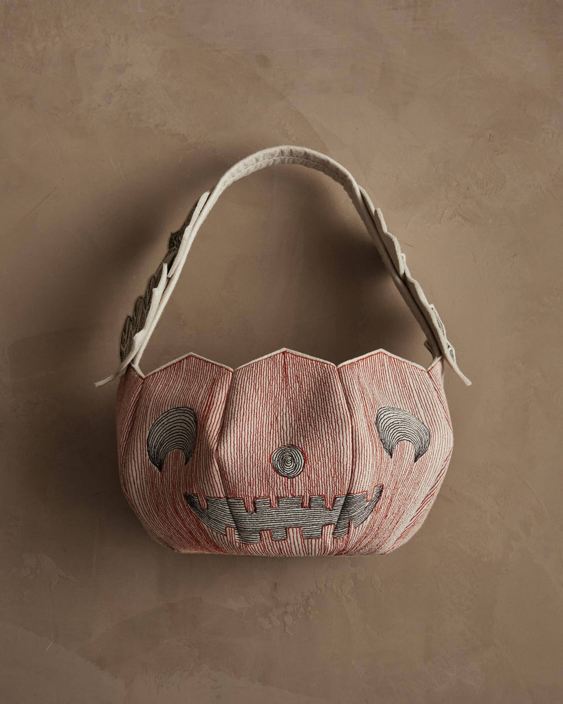 The Coral & Tusk Jack-o'-Lantern Basket features a sculpted, pumpkin-like felt shape with a stitched jack-o’-lantern face in black and red. A textured handle adds to this festive, trick-or-treat inspired design.