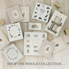 A flat lay of "Our Little Adventure at Christmas (Baby's first Christmas)"—an illustrated book with animal and nature themes for toddlers—arranged on a light wooden surface. Wooden letter blocks and "SHOP THE WHOLE COLLECTION" appear below.