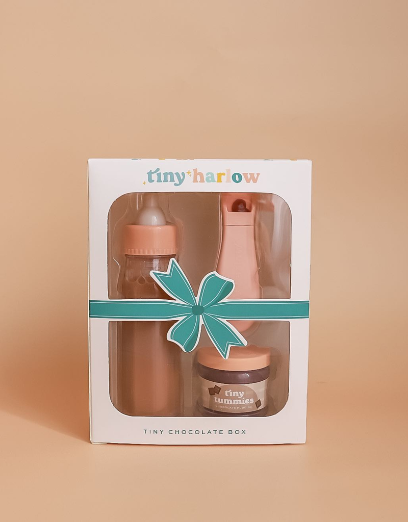 The Tiny Harlow gift box, an ideal choice for Tiny Tummies, features toy baby items such as a puree and milk bottle set in chocolate for dolls. The box is beautifully decorated with a blue ribbon graphic set against a peach background.