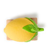 A yellow, lemon-shaped Lou The Lemon Baby Car made of natural rubber with green leaves sits atop a small rectangular wooden block, viewed from above against a white background.