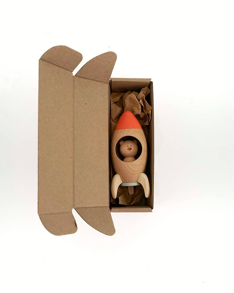 The Sabo Concept Rocket with Bear, a small wooden space toy featuring a cute bear inside, arrives in an open cardboard box with brown packing paper, ready for imaginative play.