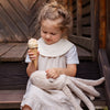 A young girl in a light dress sits on wooden steps, holding a Senger Naturwelt Cuddly Animal - Octopus for comfort as she admires an ice cream cone with sprinkles in her hand.