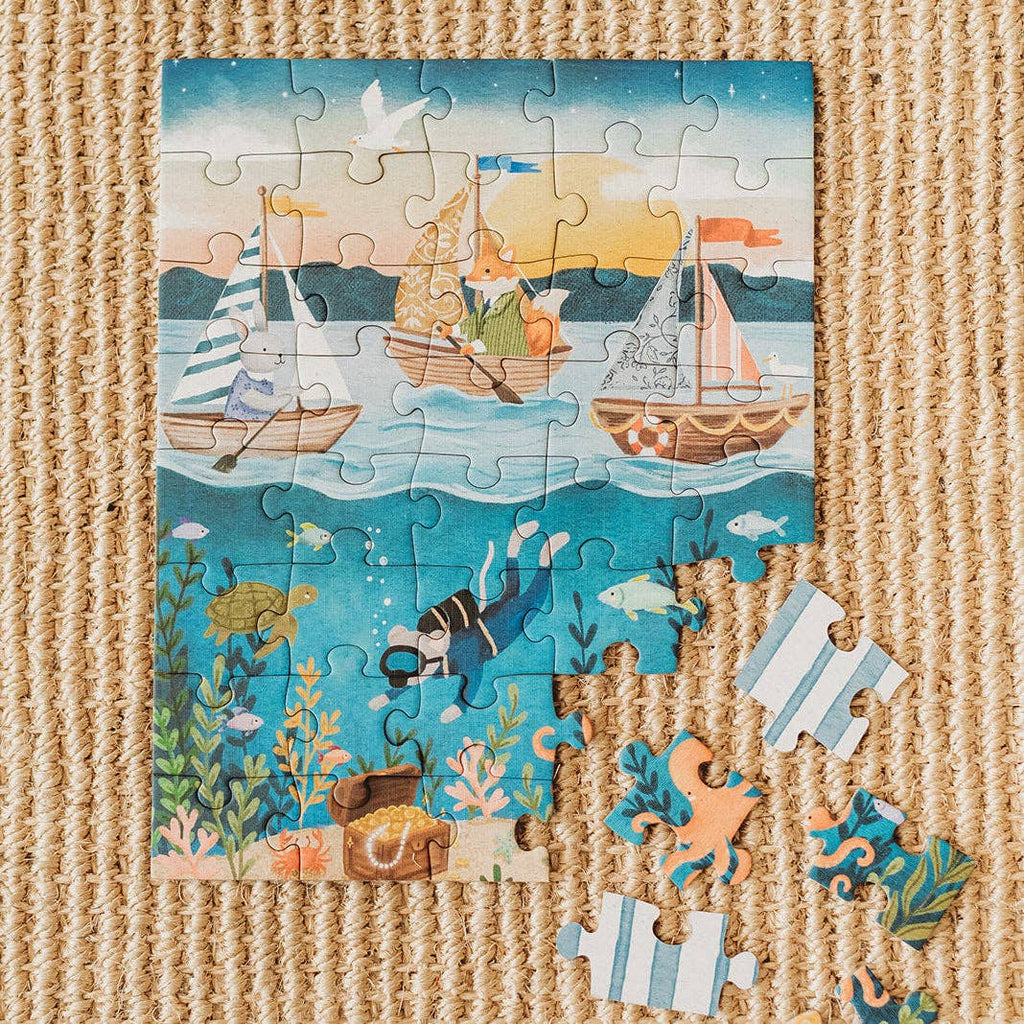 A partially completed Ocean Explorers 40 Piece Mini puzzle is displayed on a woven mat, featuring sailing animals above the water and a diver, turtle, and sea creatures below. Four pieces are set aside in this engaging kids’ jigsaw puzzle.