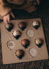 A child’s hand hovers over the My Little Lady Bug Wooden Puzzle—a Montessori counting toy featuring numbered slots and ladybug-shaped pieces in various shades of brown and beige. The board rests on a textured brown surface.